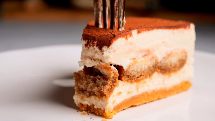 Slice of creamy tiramisu cheesecake on a white plate with a fork