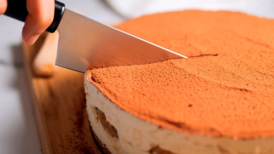 Cutting a tiramisu cheesecake cake with a knife.