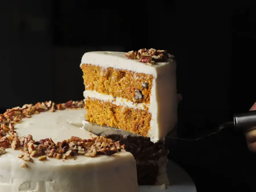 Carrot cake slice with frosting and nuts on a cake server.
