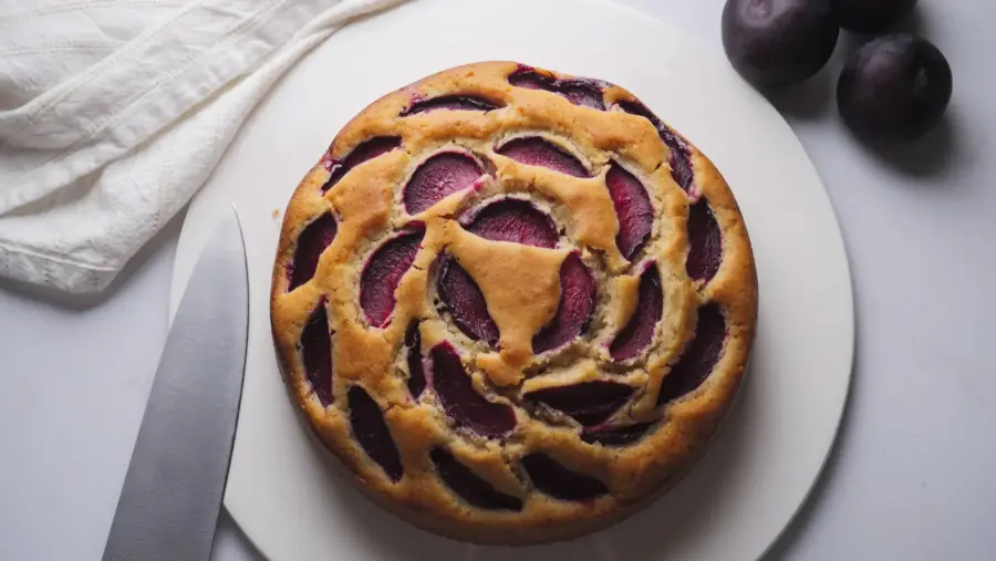 Plum Cake on a cake plate with a knife and some plums