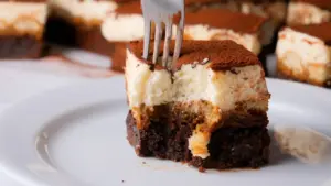 Fork in creamy tiramisu brownies slice on white plate.