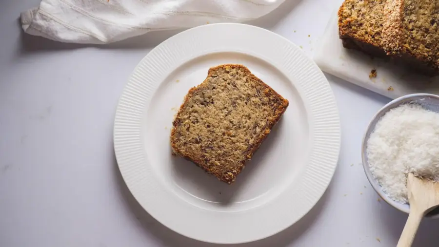 Moist Coconut Banana bread slice on a white plate with coconut flakes.