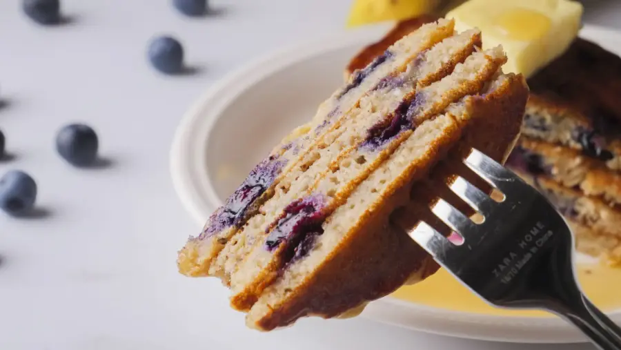 Blueberry pancakes on fork, close-up with fresh berries.