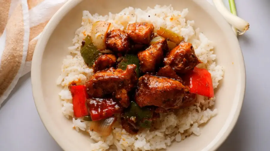 Spicy black pepper chicken stir-fry on white rice with black peppers, bell peppers, and onions in a bowl.