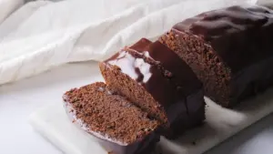 Chocolate cake loaf with glossy icing, sliced on a white marble board.