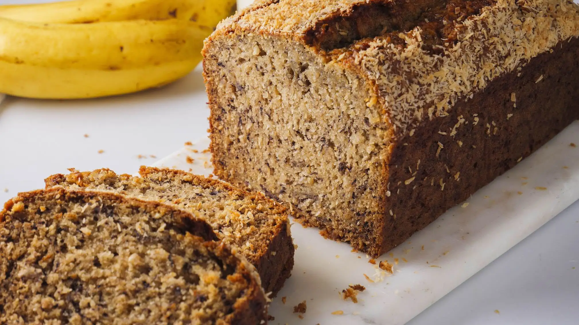 Coconut Banana bread loaf with slices on a marble board.