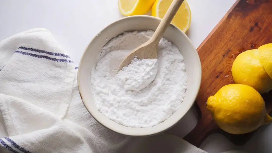 A bowl of powdered sugar with lemons and a wooden spoon on the table.