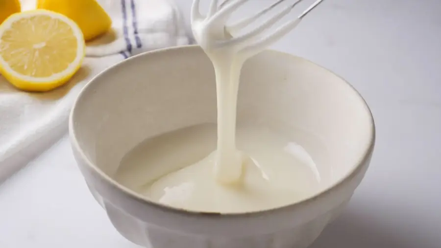 Easy lemon glaze in a bowl with fresh lemon slices nearby.