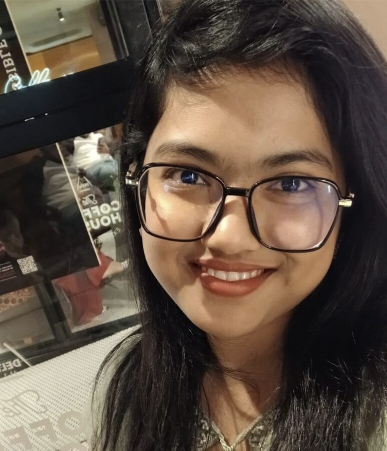 Smiling woman with glasses in a coffee shop.