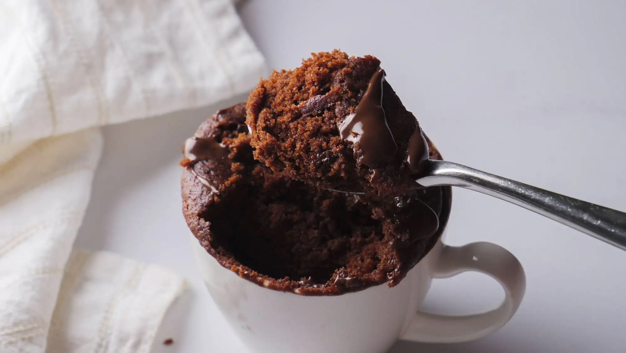 Chocolate mug cake with melting chocolate on a spoon.