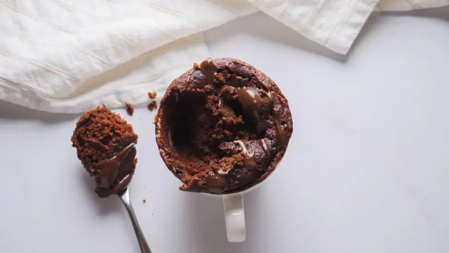 Nutella mug cake with melted chocolate, spoonful taken out on a white background.