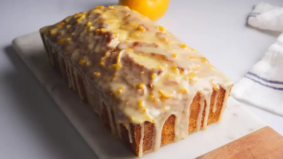 Glazed orange loaf cake on a marble surface.