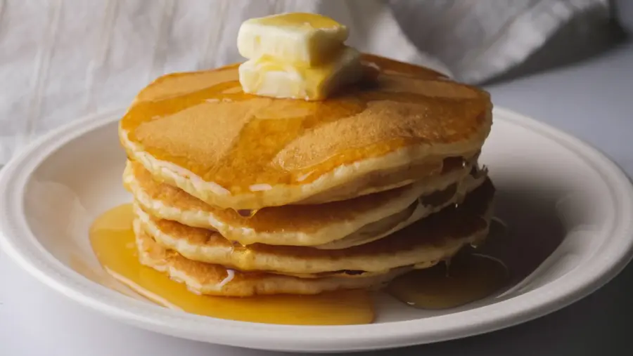 Stack of pancakes without milk, with honey and butter on a white plate.