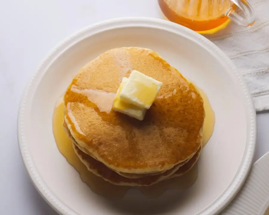 Stack of pancakes without milk, with syrup and butter on a white plate.