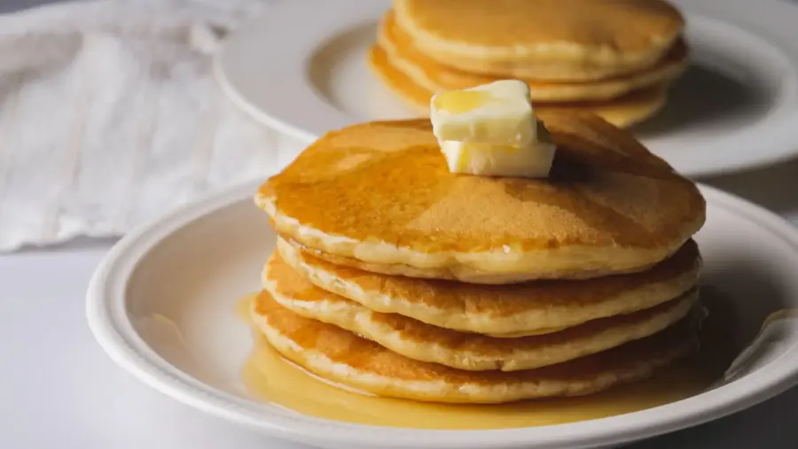 Stack of pancakes without milk, with syrup and butter on a white plate.