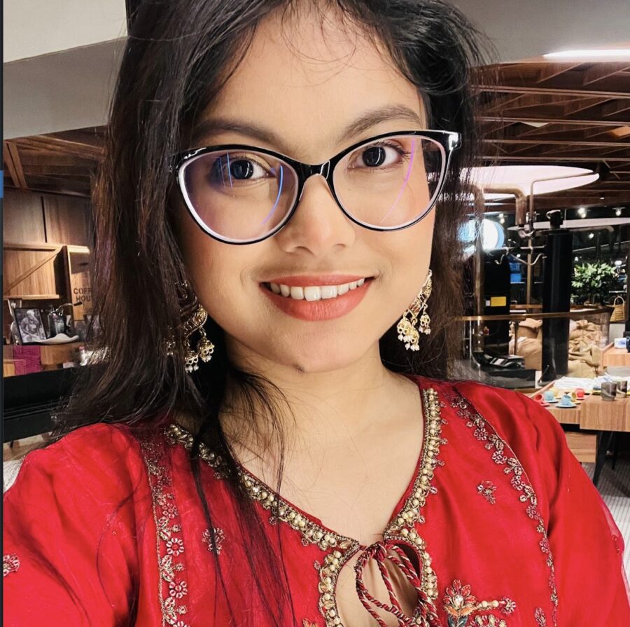 Smiling Rima in a red dress with glasses and earrings.