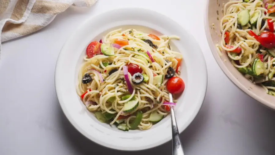 Fresh spaghetti salad with veggies in a white bowl.