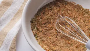 Homemade Steak Seasoning spice blend in a bowl with a whisk on a towel.