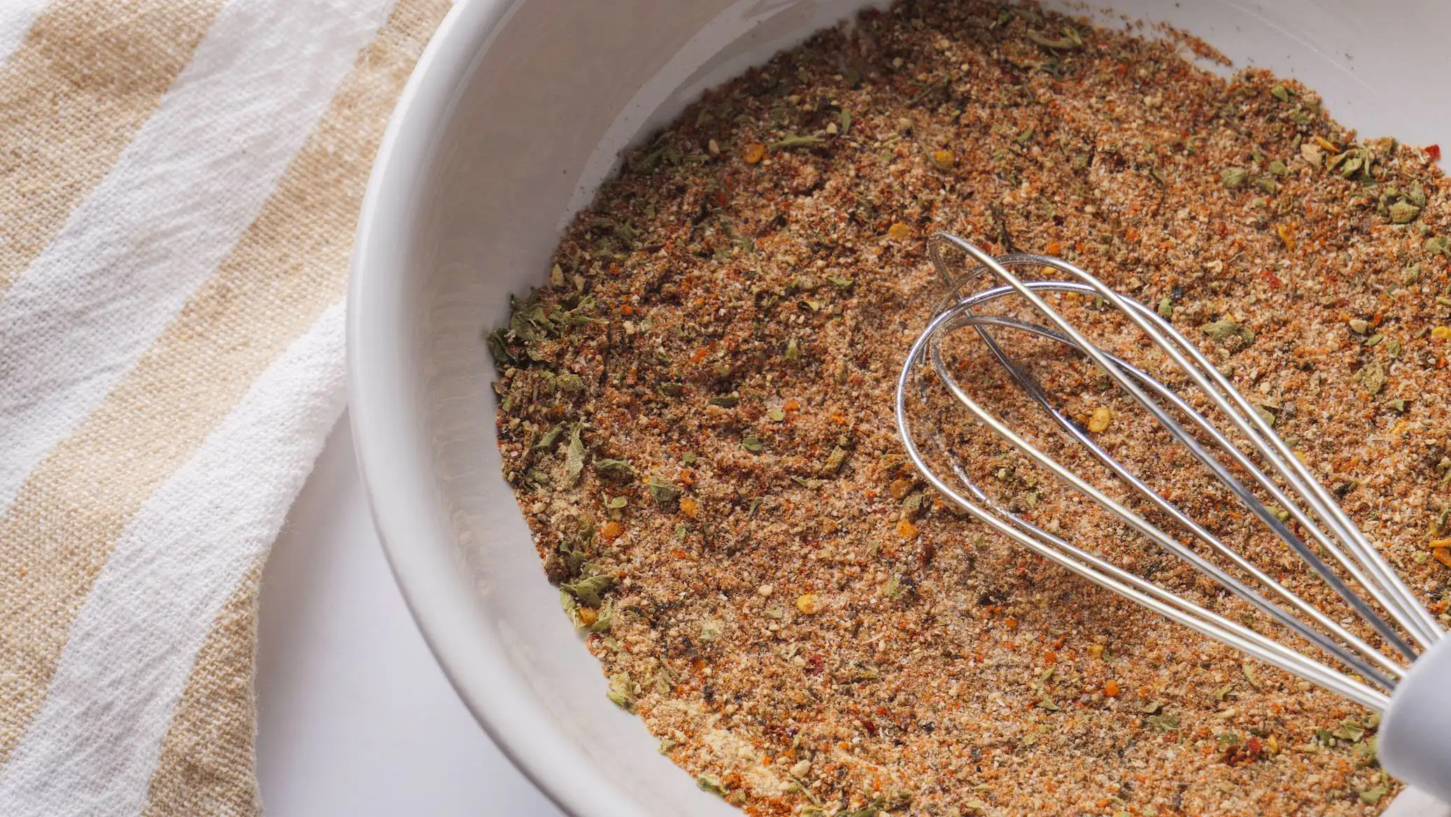 Homemade Steak Seasoning spice blend in a bowl with a whisk on a towel.