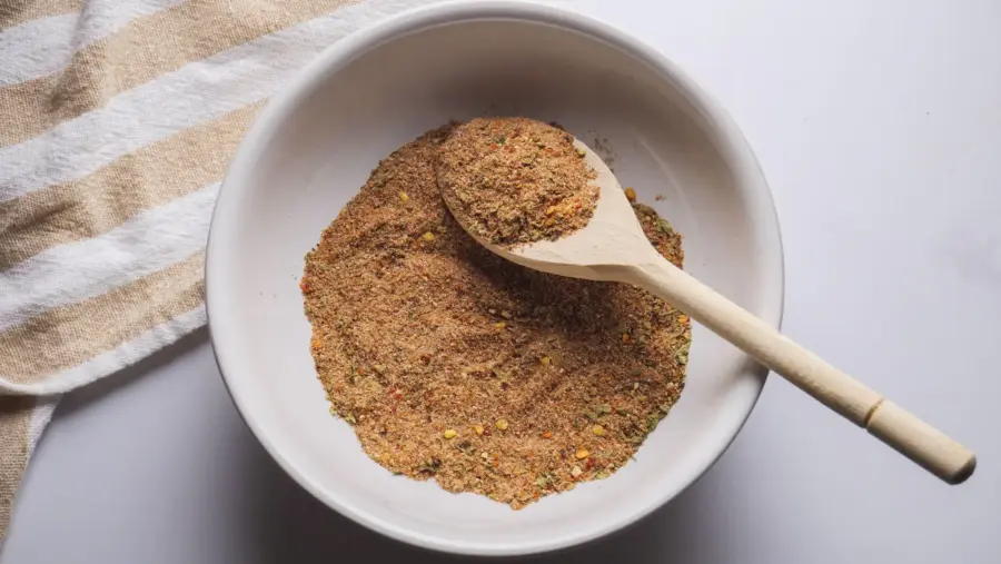 Bowl of mixed steak spices with wooden spoon on striped cloth