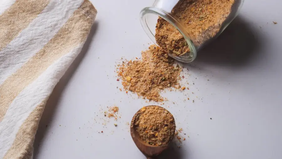 Spilled Steak rub spice mix from the glass jar onto the table with a cloth.