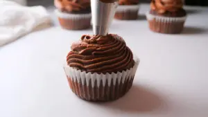 Chocolate cupcake being frosted with swirls of rich chocolate cream cheese icing.