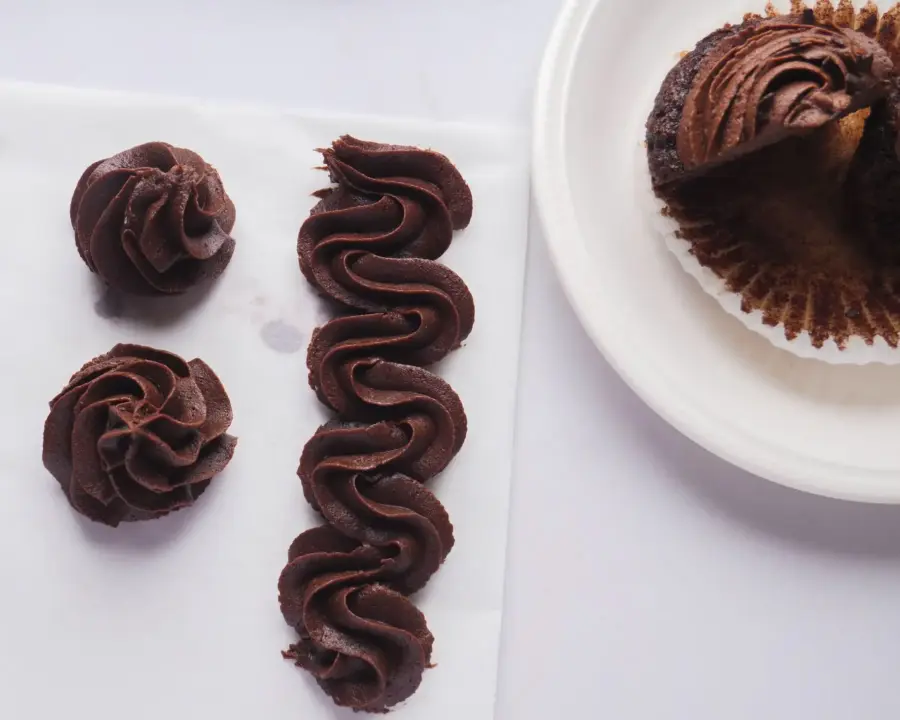 Chocolate cupcake with swirled cream cheese and chocolate icing on a plate, next to piped chocolate designs.