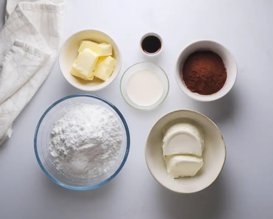 Frosting essentials: butter, cocoa powder, sugar, cream cheese, cream, and vanilla extract.