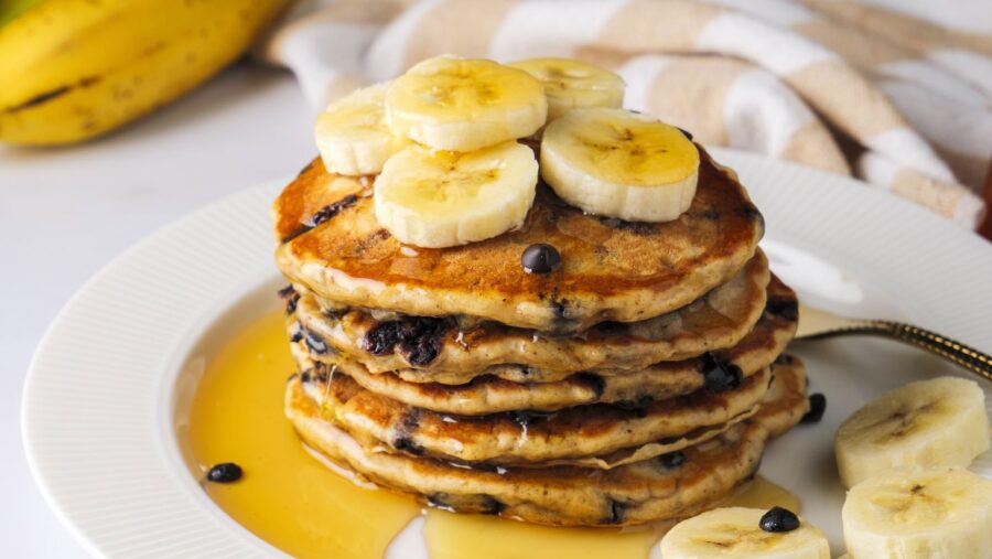 Stack of chocolate chip banana pancakes with banana slices and maple syrup