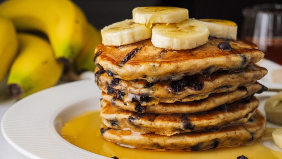 Stack of chocolate chip banana pancakes with banana slices and maple syrup