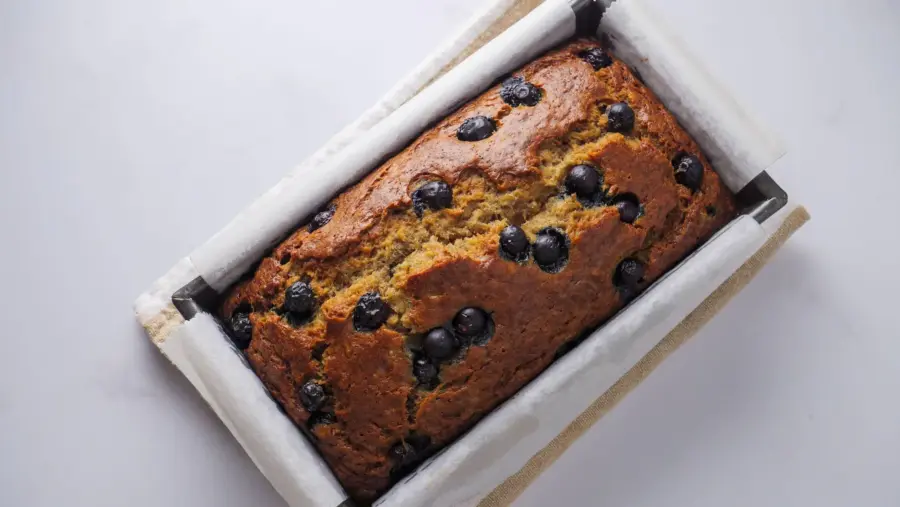 Blueberry banana bread in a baking pan on a white background.