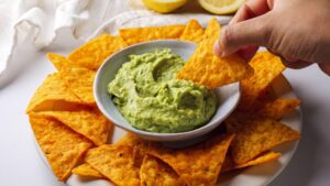 Nachos with creamy avocado sauce dip on a white plate.