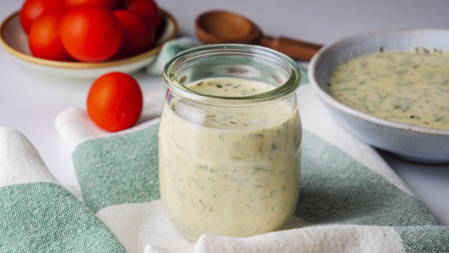 Creamy Italian salad dressing in a jar on a green checkered cloth with some tomatoes