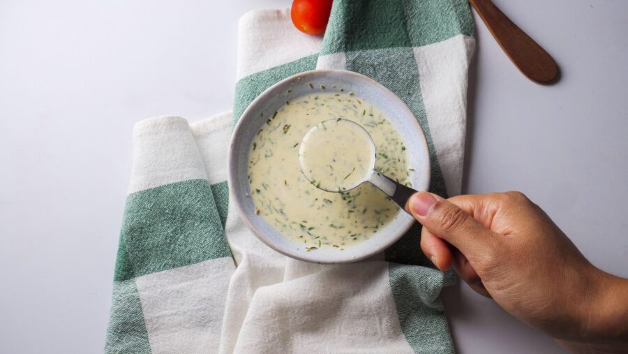 Hand holding a spoon above a homemade Creamy Italian Dressing cream soup bowl.