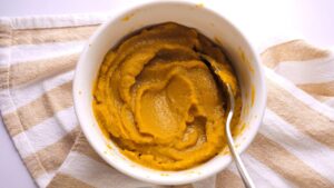 Pumpkin puree in a white bowl with a spoon on a striped cloth.