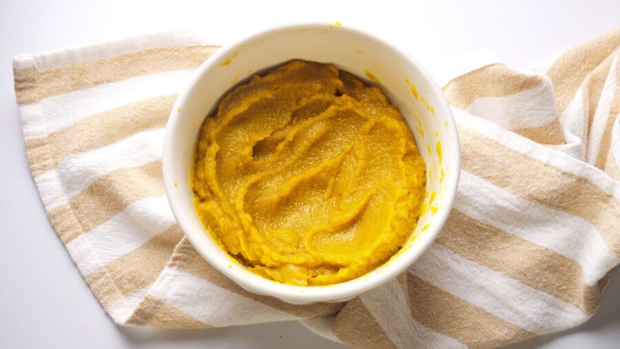 Pumpkin puree in a white bowl with a spoon on a striped cloth.