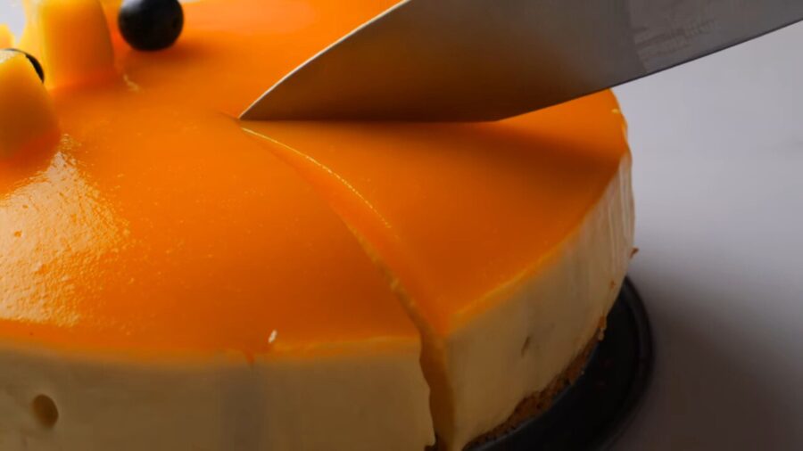 Cutting a no bake mango cheesecake with fresh fruit topping