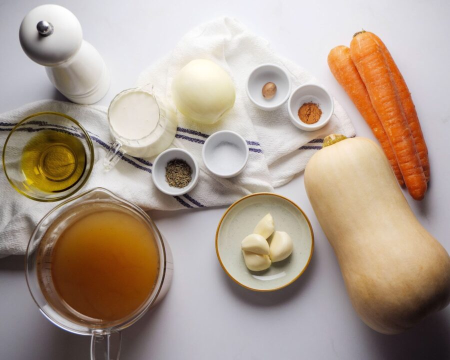 Ingredients for butternut squash soup on a white surface.