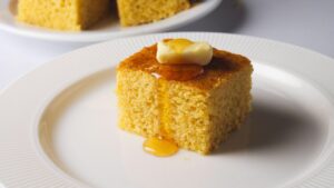 Cornbread slice with butter and syrup on a white plate.