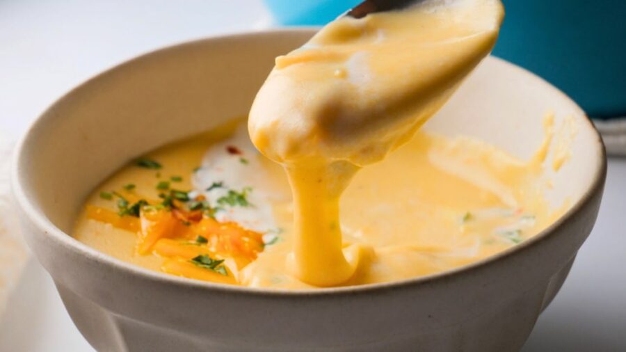 Creamy potato soup with cheese, herbs, and sour cream in a white bowl with a spoon.