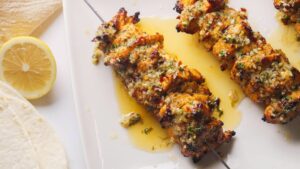 Grilled chicken skewers with herbs and lemon slices.