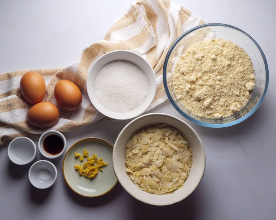 Baking ingredients on table: eggs, sugar, almonds, lemon zest.