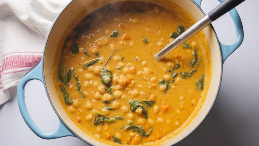 Mediterranean chickpea soup in a pot with spinach and a ladle.