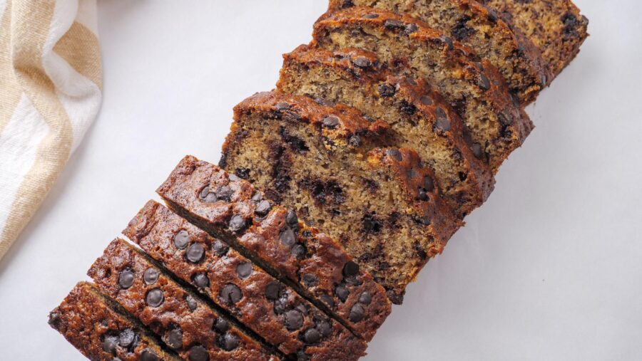 Sliced homemade banana bread with chocolate chips on a white surface.