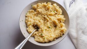 Creamy cheesy rice served in a white bowl with a spoon.