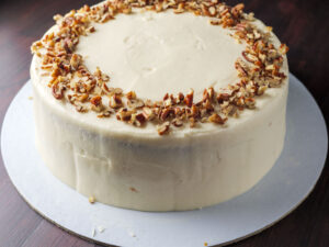 Creamy frosted cake with cream cheese frosting, topped with chopped nuts, on a plate.