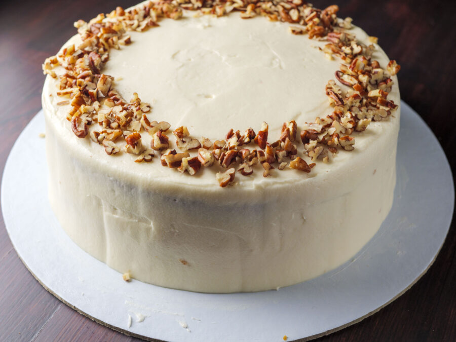 Creamy frosted cake with cream cheese frosting, topped with chopped nuts, on a plate.