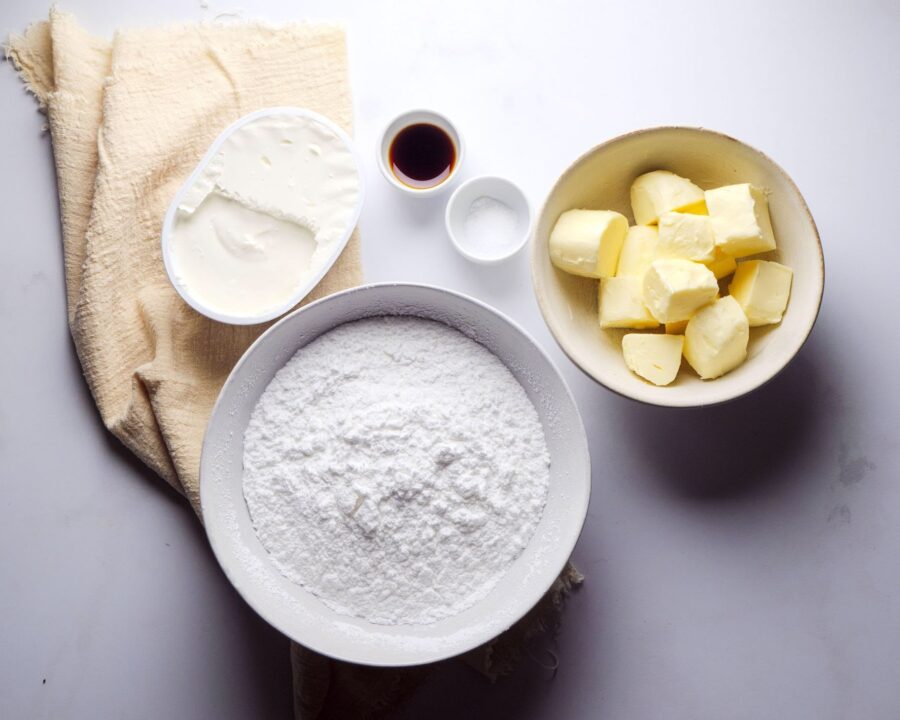Baking ingredients on a table: butter, sugar, vanilla, and cream.