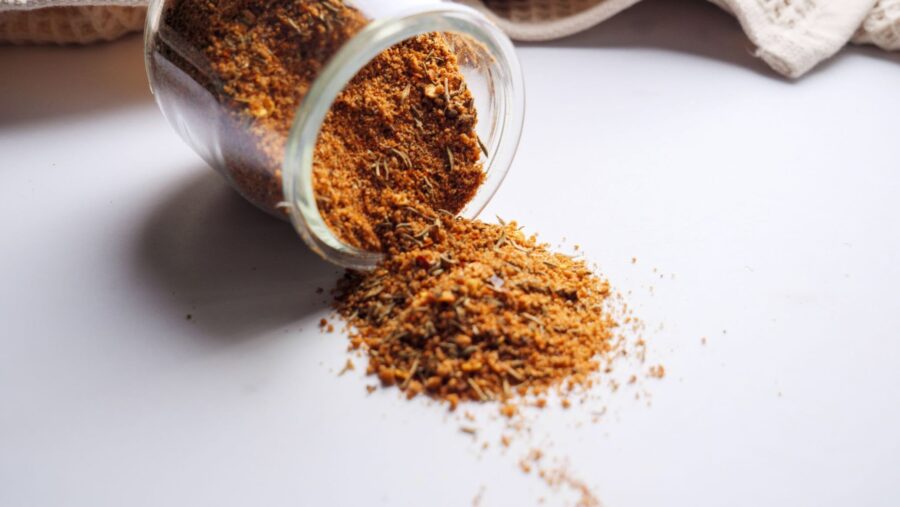 Spilled jar of aromatic jerk spice blend on white surface