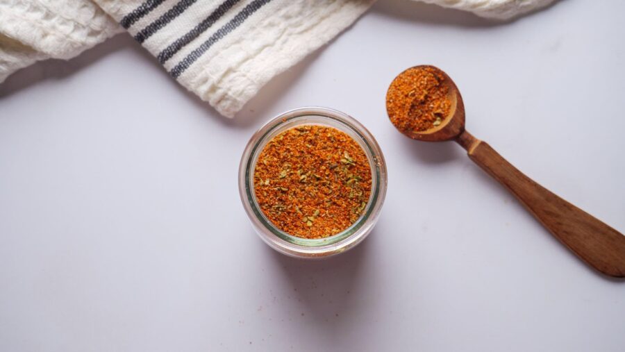 Jar and spoon filled with taco seasoning mix spices on a white background.